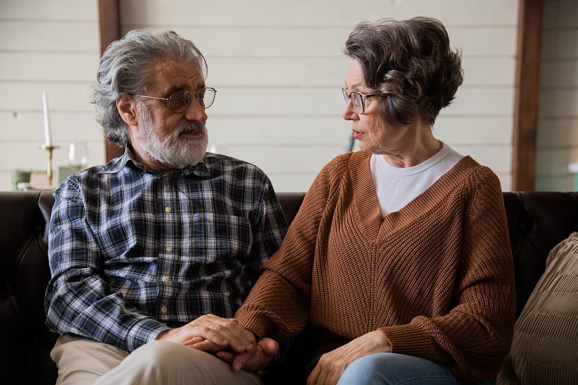 Older couple holding hands while sitting together on a sofa