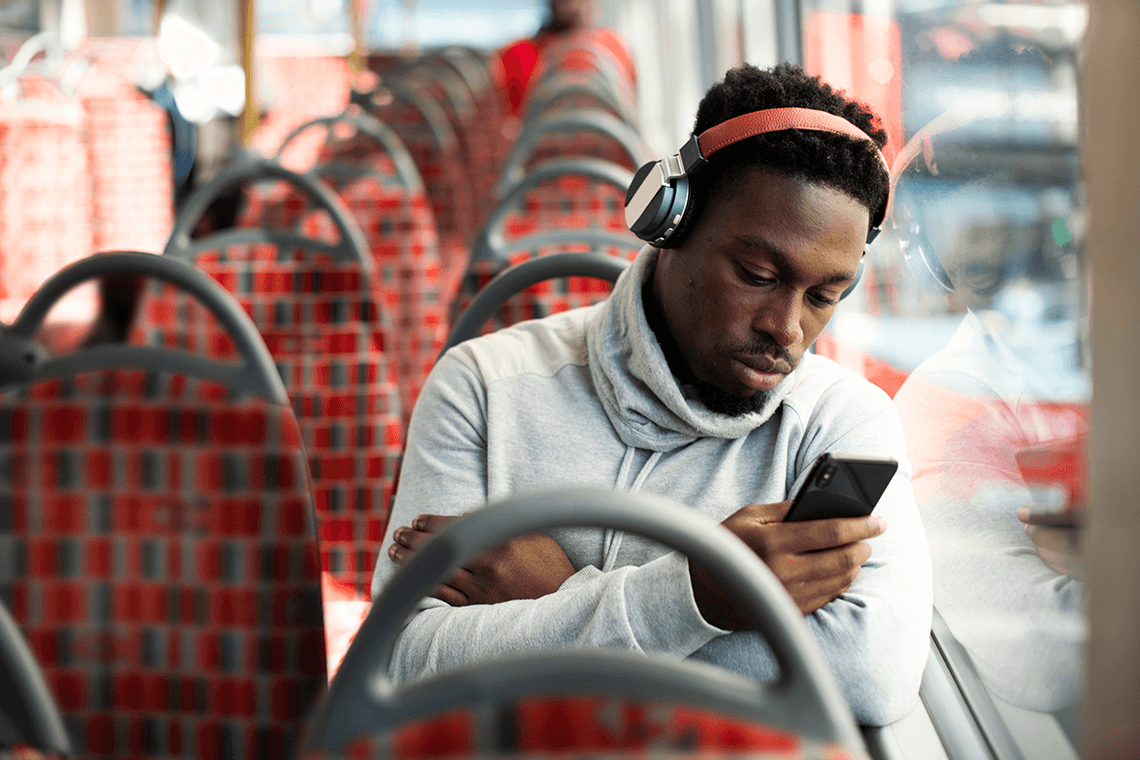 Man wearing headphones and checking his phone while riding a bus