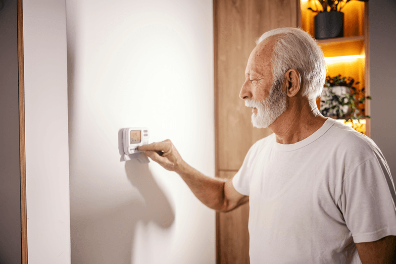 Man adjusting a thermostat to reduce utility costs