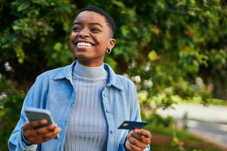 Smiling woman outdoors holding a phone and a credit card