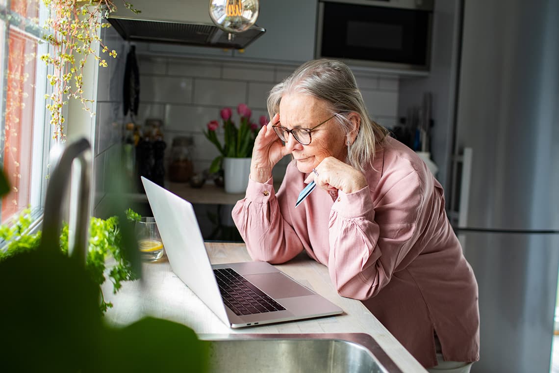 Woman looking concerned while reviewing her laptop at the kitchen counter