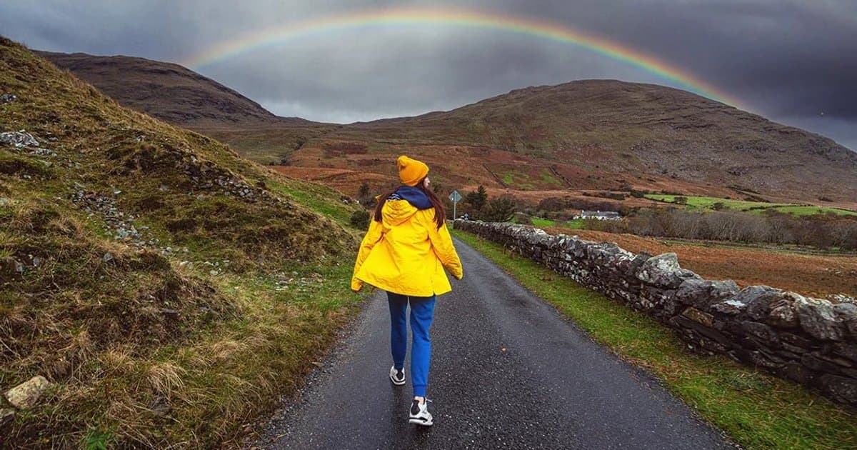Person in a yellow coat walking toward a rainbow