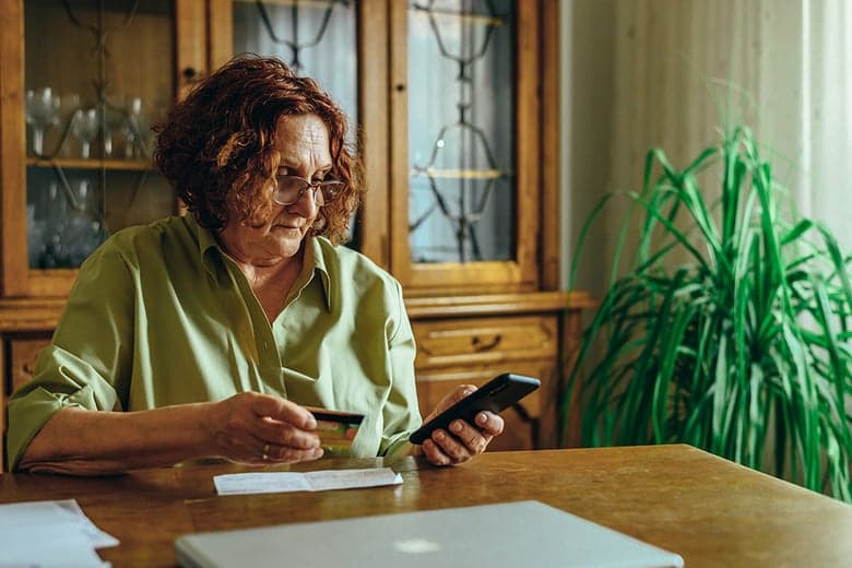 Woman at home reviewing a bill while holding a credit card and phone