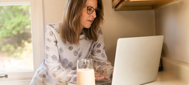 Woman with glasses working on laptop with a glass of milk